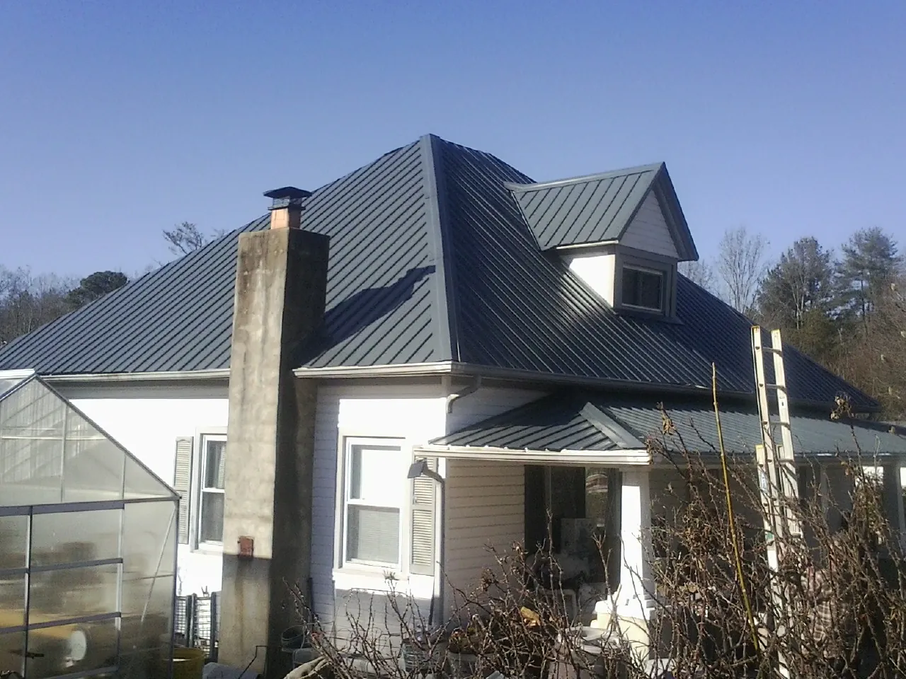 Dark blue standing seam metal roof on a white farmhouse with dormer — Slate & Tile Roof Repair by Roofing Brothers in Gum Spring