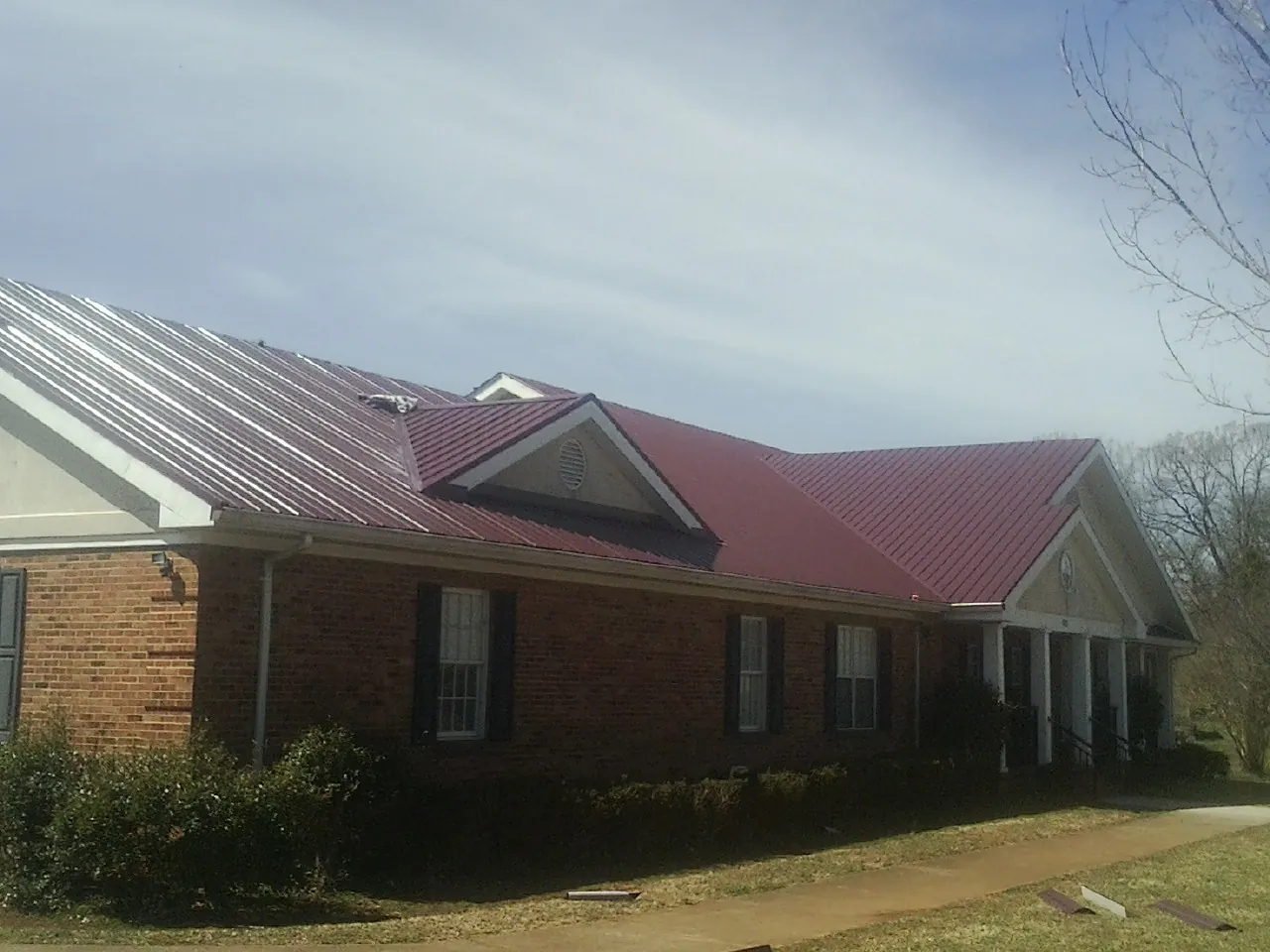 Red metal roof with gabled entries on a long brick building, from a Hail Damage Roof Repair job in Gum Spring
