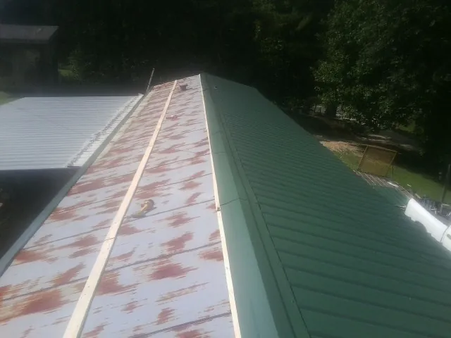 Old rusted panels beside newly installed green metal roofing — Wind Damage Roof Repair by Roofing Brothers in Gum Spring