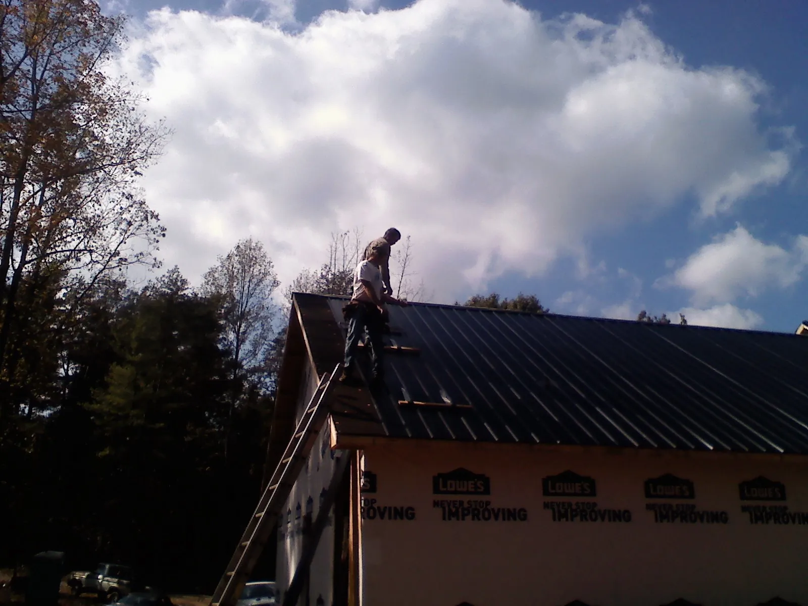 Roofer fastening dark metal panels high against a cloudy sky, from a Roof Inspection job in Gum Spring